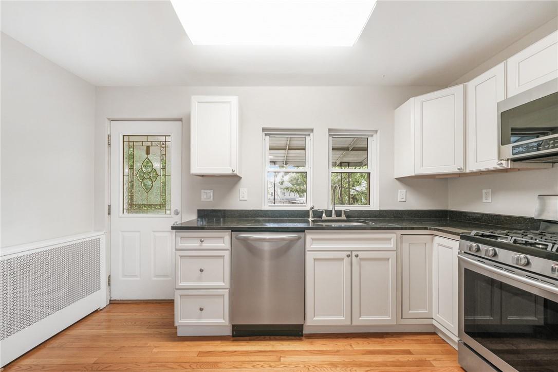 Kitchen with sink, light hardwood / wood-style flooring, radiator heating unit, white cabinetry, and stainless steel appliances