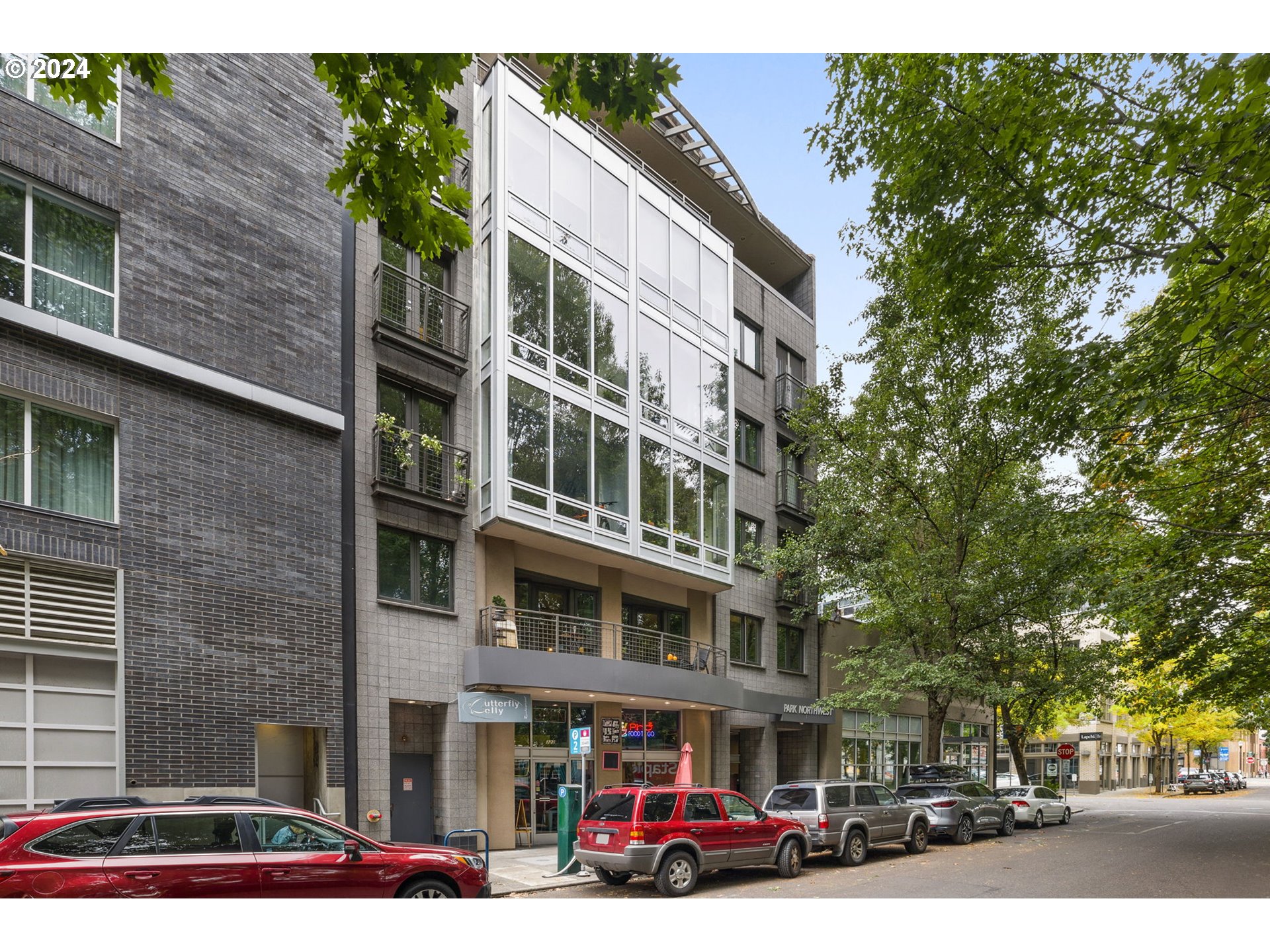 a front view of a building with lot of cars and trees