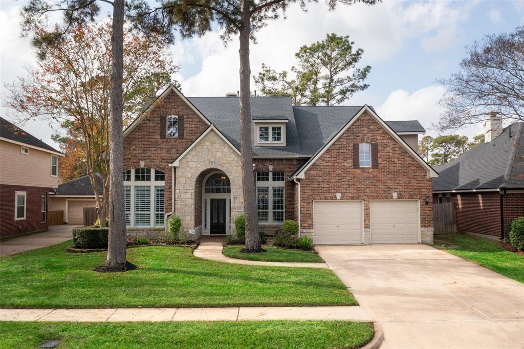 This charming two-story brick home features a welcoming portico and elegant windows. It includes a spacious two-car garage, a well-maintained lawn, and mature trees, offering great curb appeal in a quiet neighborhood.