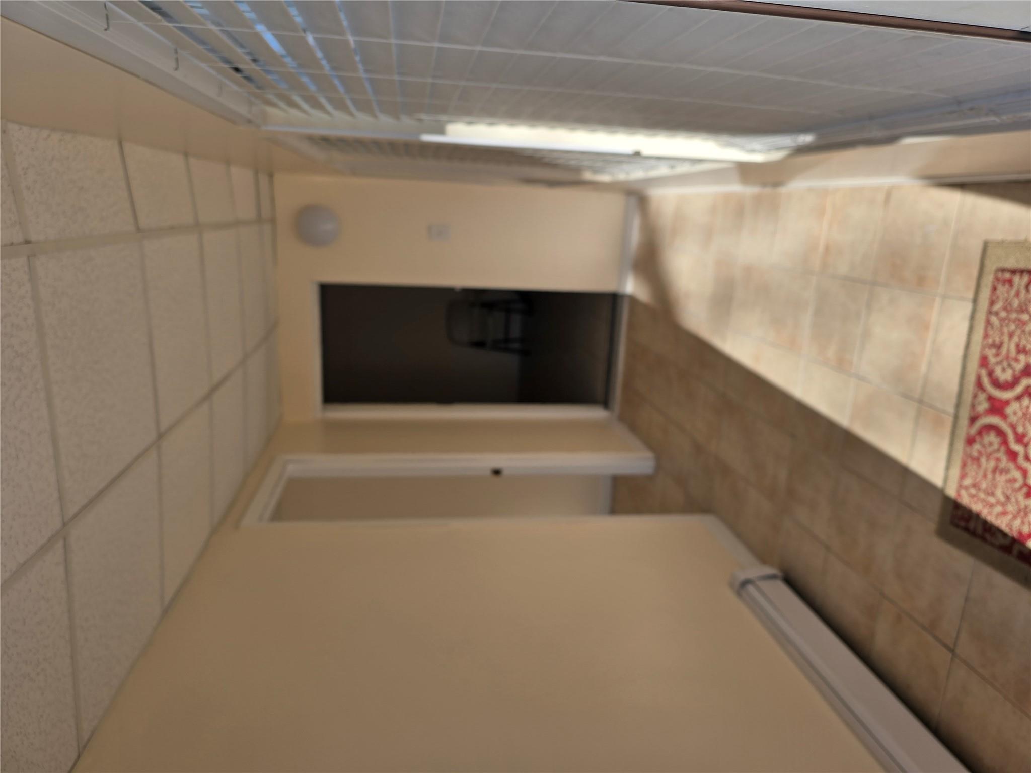 Hall with tile patterned floors, a drop ceiling, and a baseboard heating unit