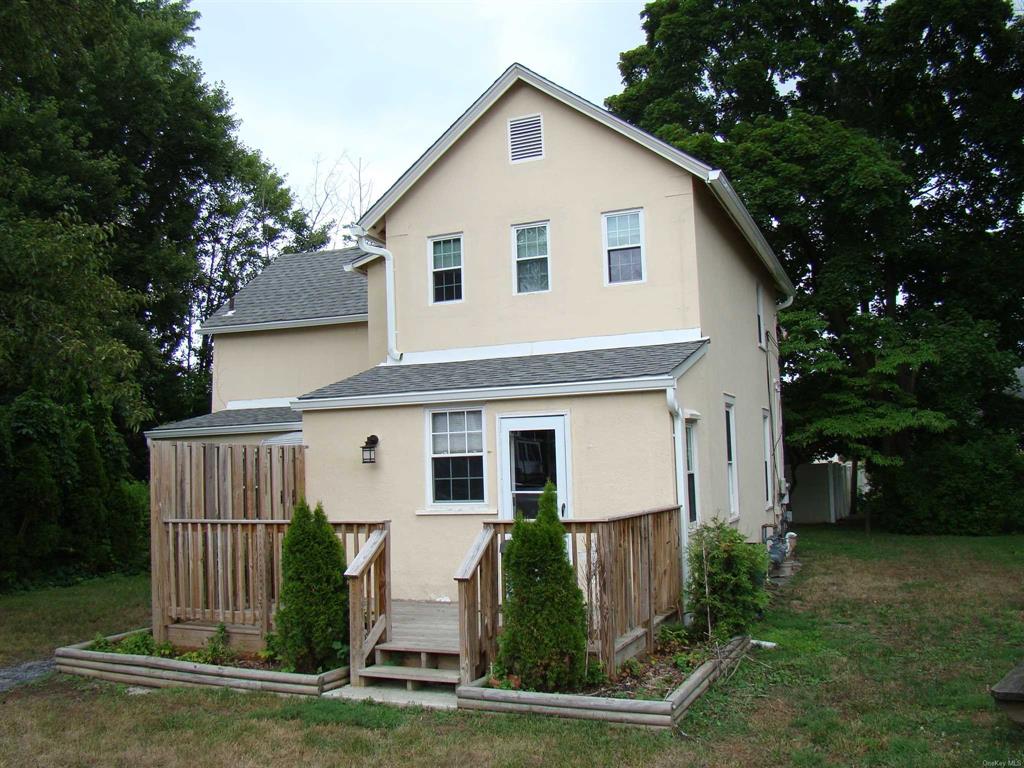 a view of a white house in front of a yard with plants and large tree