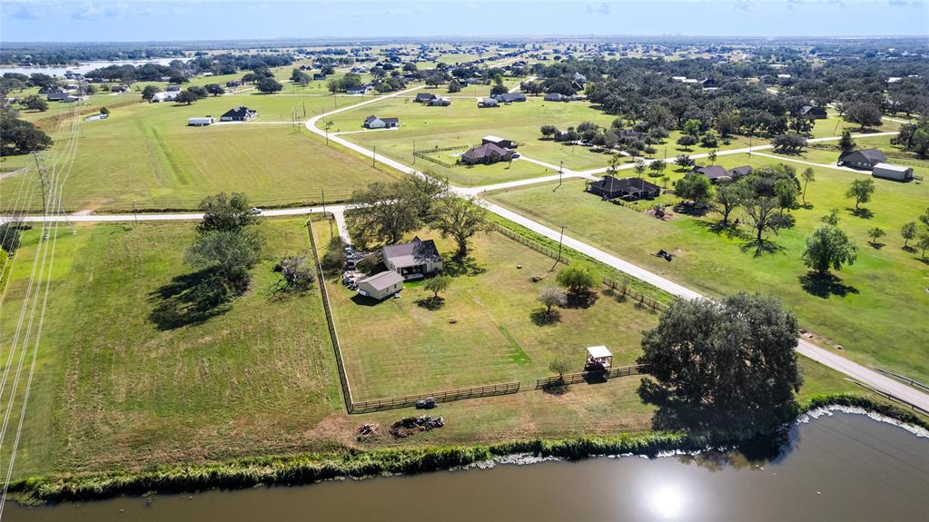 This photo showcases a spacious rural property with a charming house, surrounded by open green fields and a fenced yard. The property is bordered by a road and a small waterway, offering a serene and expansive setting ideal for those seeking tranquility and space.