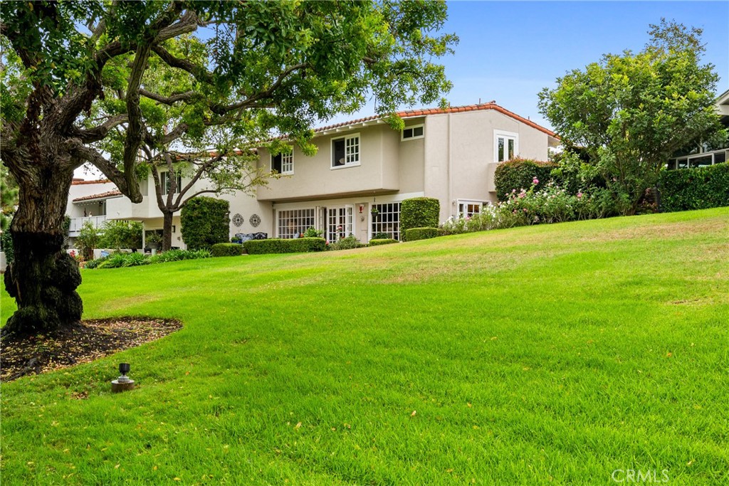 a white house with a big yard plants and large trees