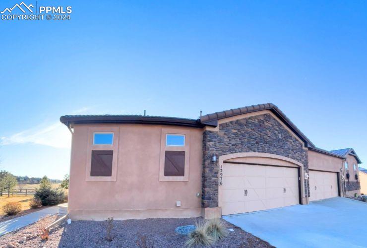 Stucco-front patio home featuring a tile roof, a spacious two-car garage and well-maintained landscaping