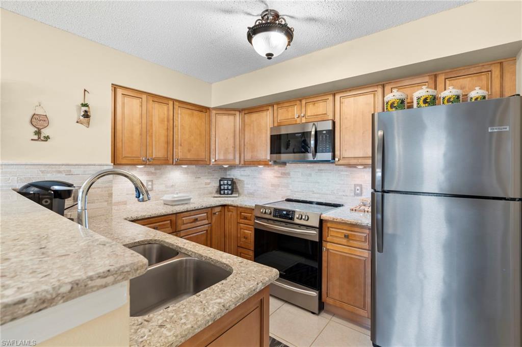 Kitchen with a textured ceiling, tasteful backsplash, stainless steel appliances, light tile patterned floors, and light stone countertops