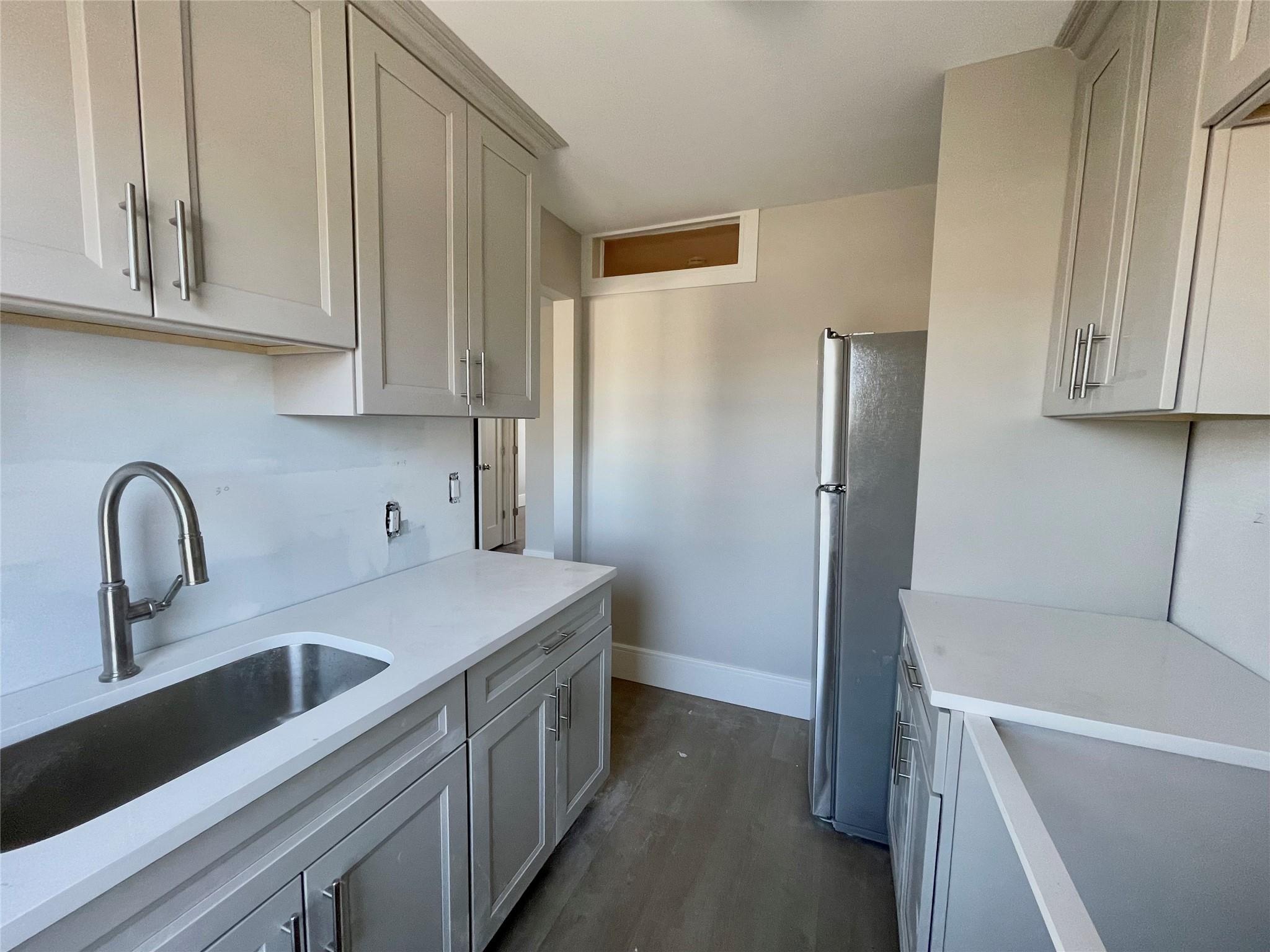 Kitchen featuring gray cabinetry, stainless steel refrigerator, dark wood-type flooring, and sink