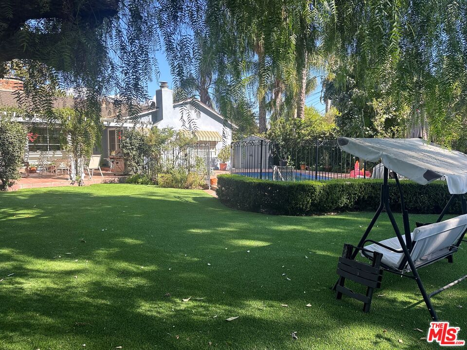 a view of a backyard with table and chairs potted plants and large tree