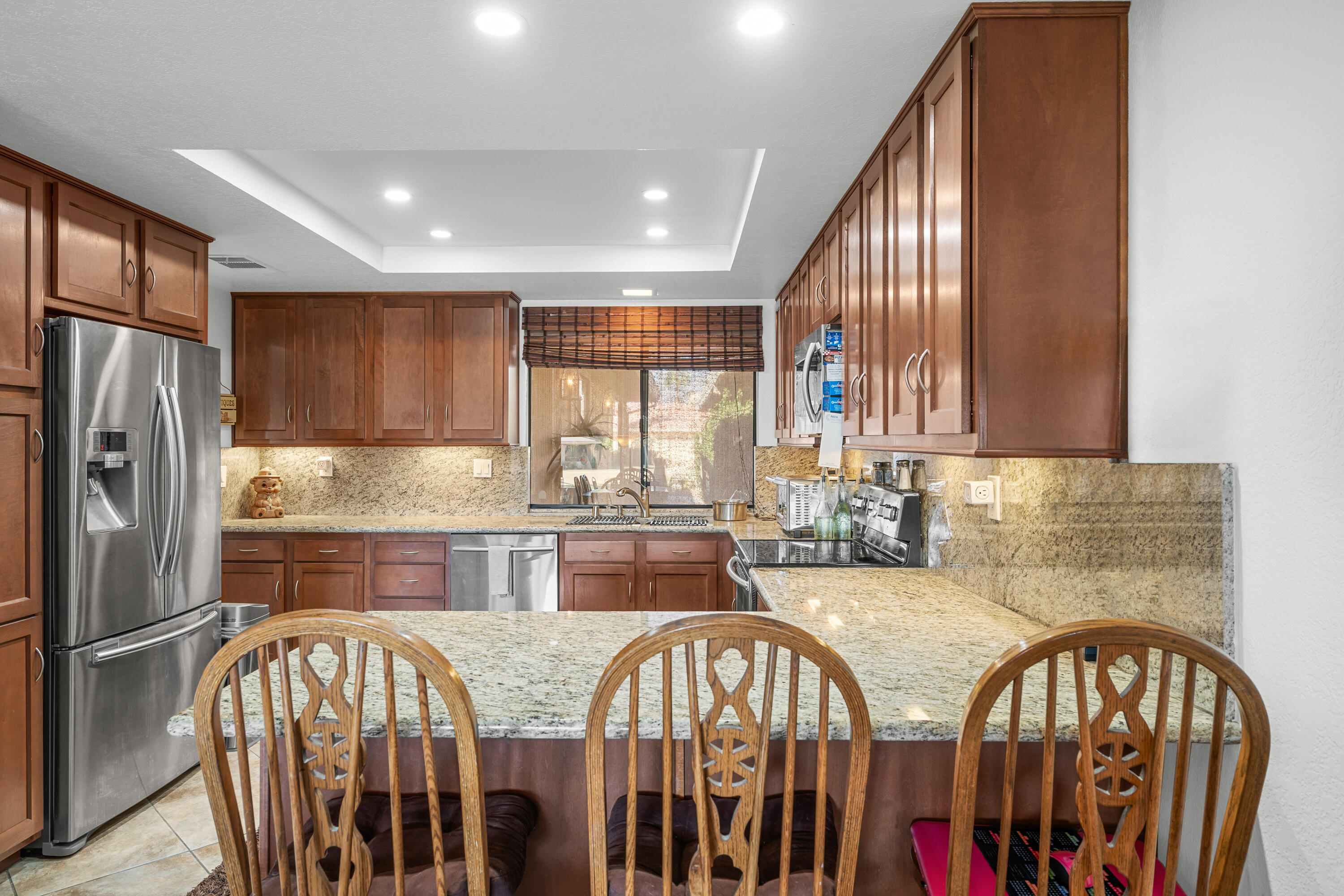 a kitchen with stainless steel appliances granite countertop a refrigerator a sink a stove a dining table and chairs