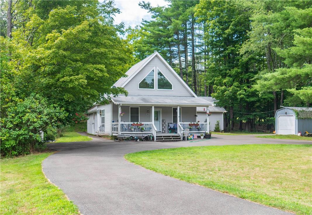 Country-style home with covered porch, an outdoor structure, a garage, and a front lawn