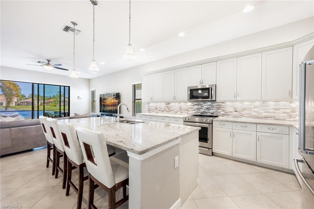 Kitchen featuring sink, stainless steel appliances, pendant lighting, white cabinets, and a kitchen island with sink