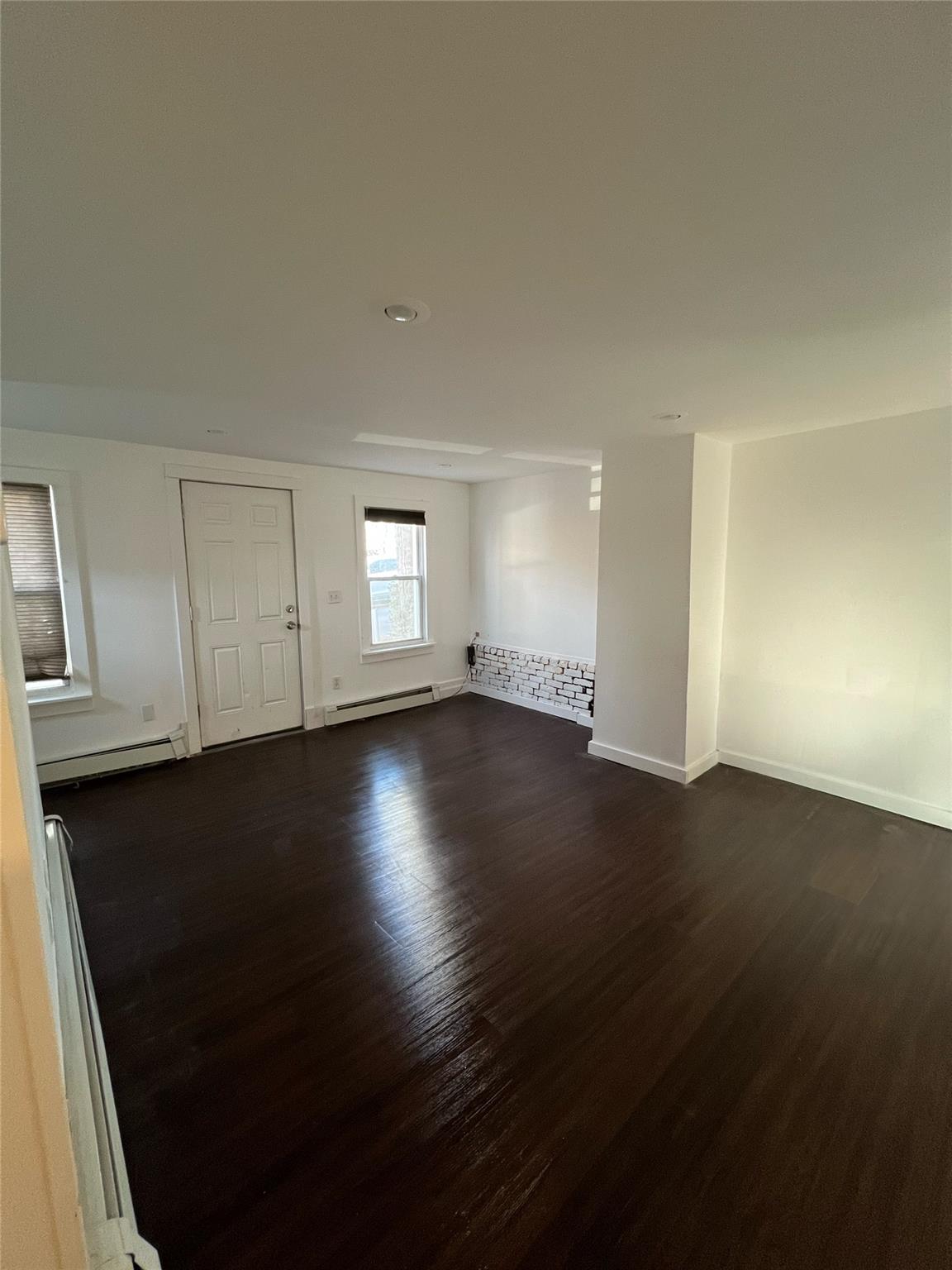 Unfurnished living room featuring baseboard heating and dark wood-type flooring