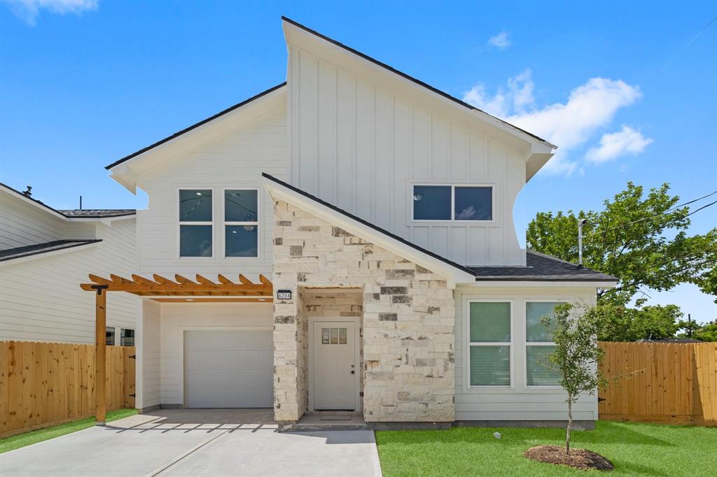 Modern two-story home with a mix of white siding and natural stone accents, featuring a single-car garage, prominent windows for natural light, and a covered entryway, all within a freshly landscaped, fenced yard.