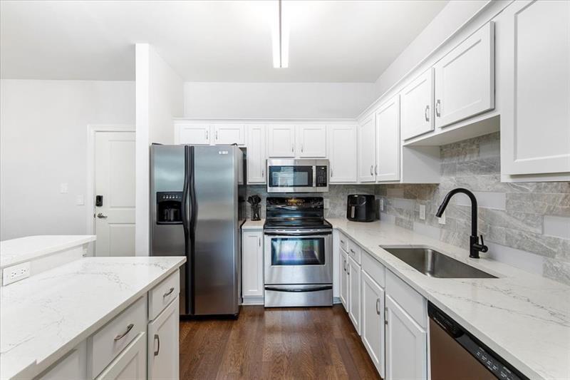 a kitchen with stainless steel appliances granite countertop a sink dishwasher a refrigerator and a stove with wooden floors