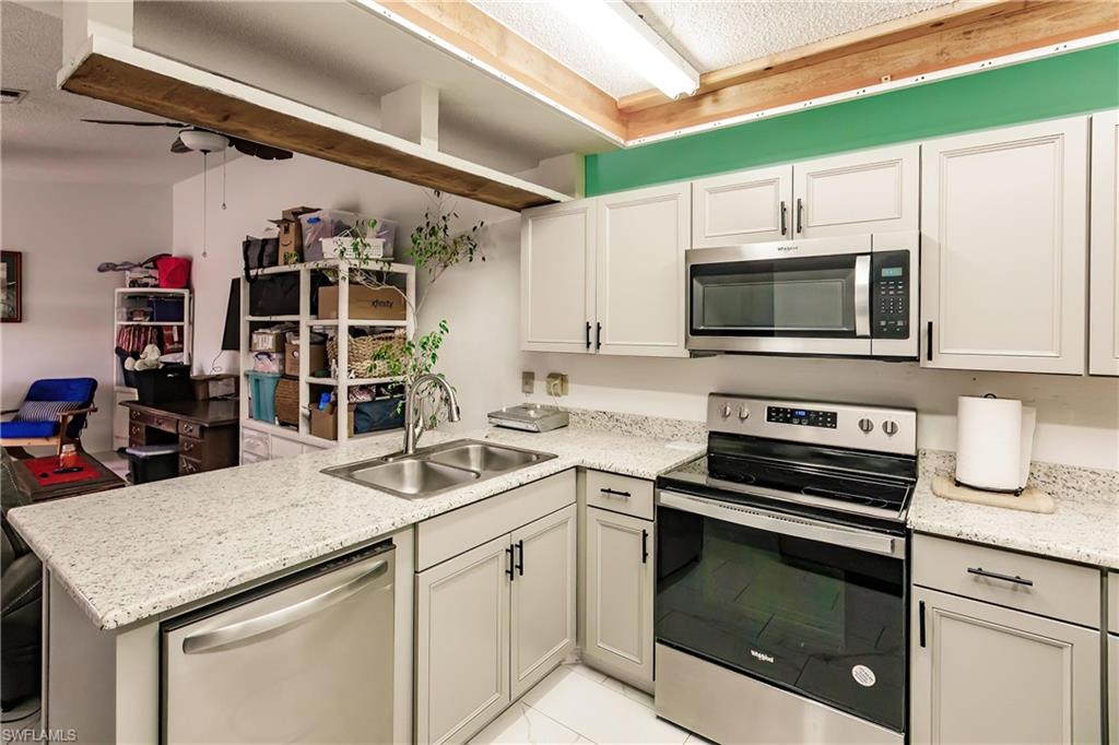 Kitchen with light stone countertops, kitchen peninsula, stainless steel appliances, light tile floors, and sink