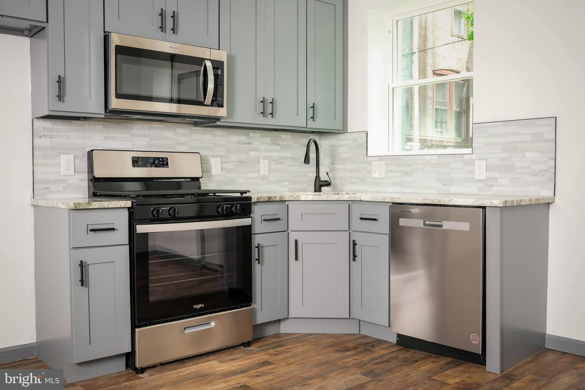 a kitchen with granite countertop white cabinets stainless steel appliances and wooden floor