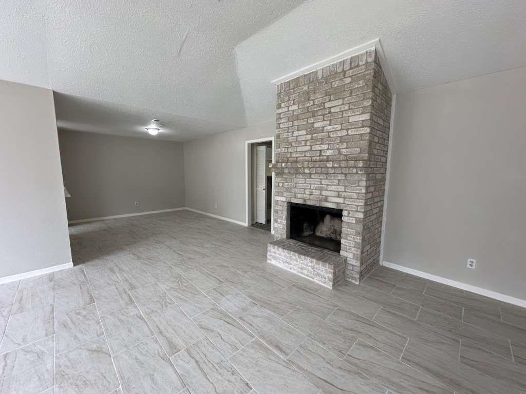 a view of an empty room with wooden floor fireplace and a window