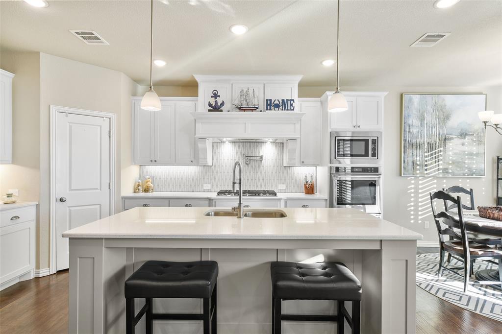 a kitchen with a dining table chairs stove and white cabinets with wooden floor