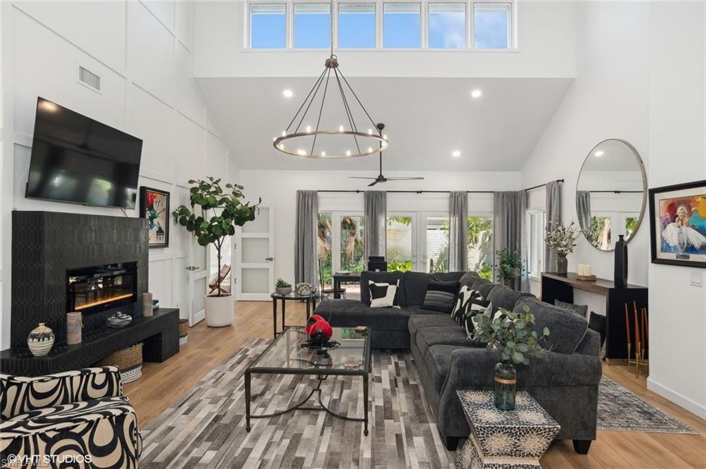 Great room featuring high vaulted ceiling, ceiling fan with chandelier, a electric fireplace, and LVT flooring.