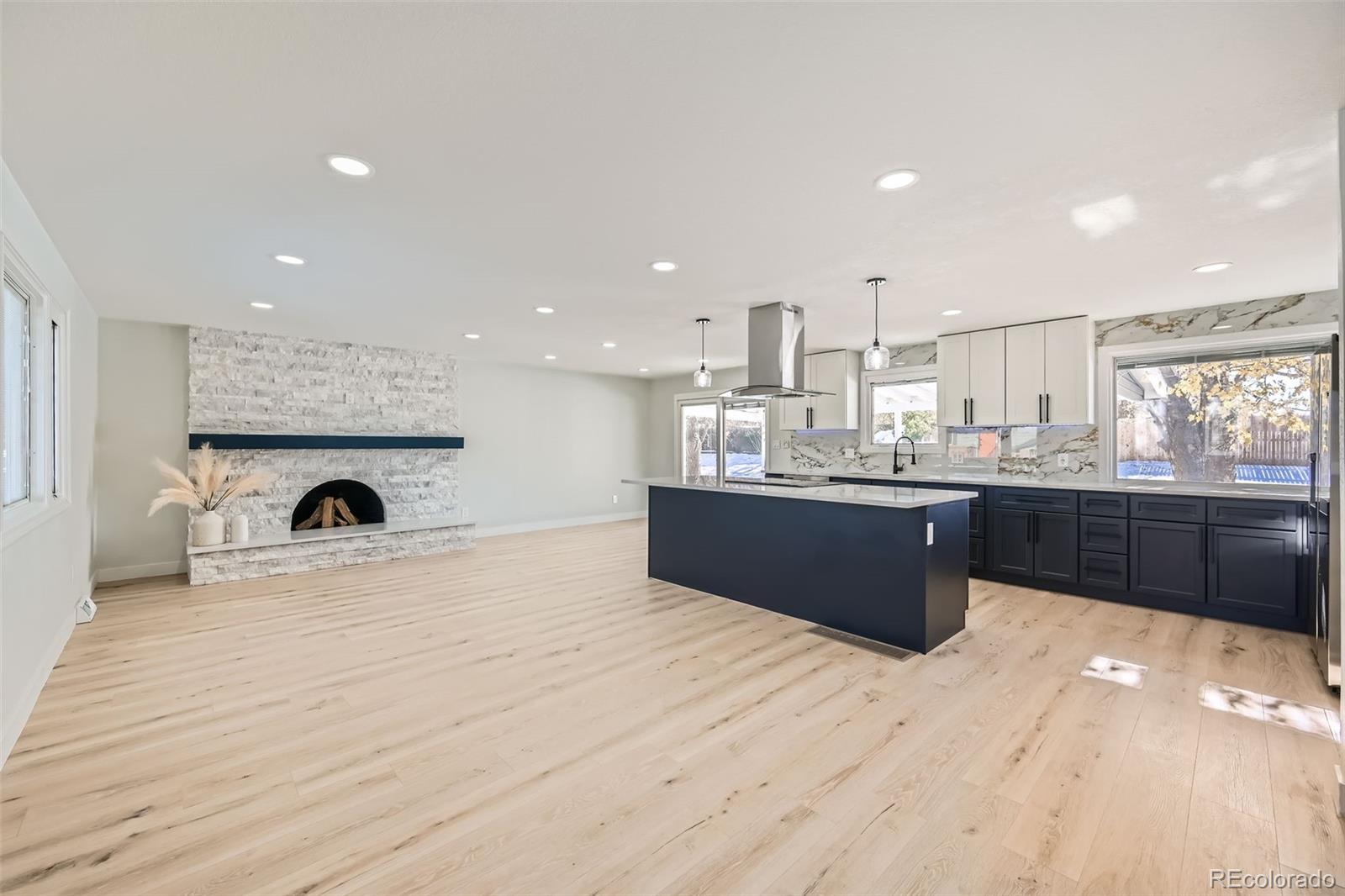 a large white kitchen with a stove a sink dishwasher and a fireplace with wooden floor