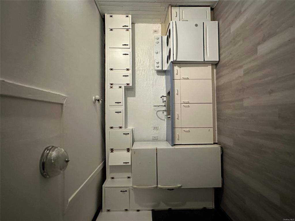 Kitchen featuring stove, wood-type flooring, sink, fridge, and white cabinetry