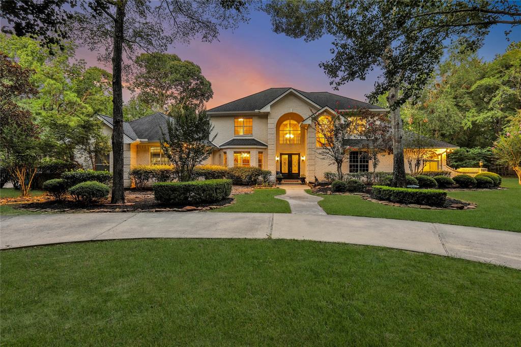 This photo showcases a spacious two-story home with an inviting exterior, featuring large windows and a well-manicured front yard with mature trees. The home is lit with warm lighting, adding to its curb appeal during the evening hours.