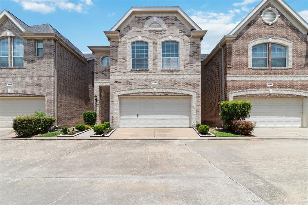 Discover your dream home in this elegant three-story brick residence, boasting a spacious two-car garage and a charming covered entrance accented by neatly-trimmed bushes and crisp white stonework.