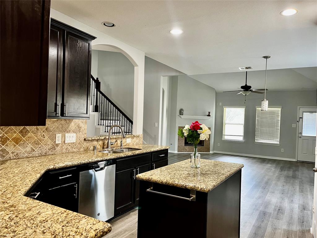 a kitchen with stainless steel appliances granite countertop a sink dishwasher and a wooden floor