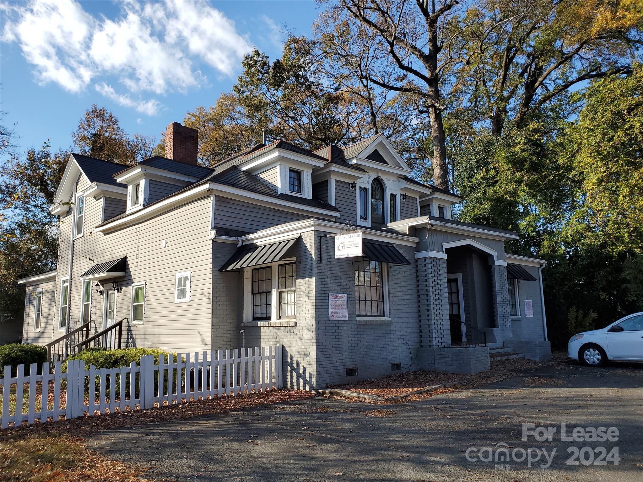 a view of a white house with large tree and wooden fence