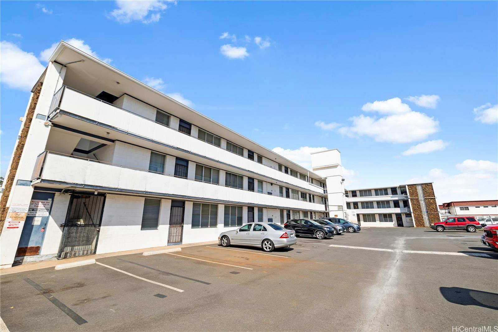 a front view of a building with lot of cars and trees