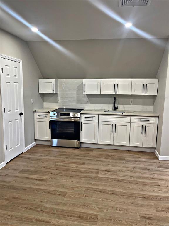 Kitchen with light hardwood / wood-style floors, stainless steel range oven, white cabinetry, and sink