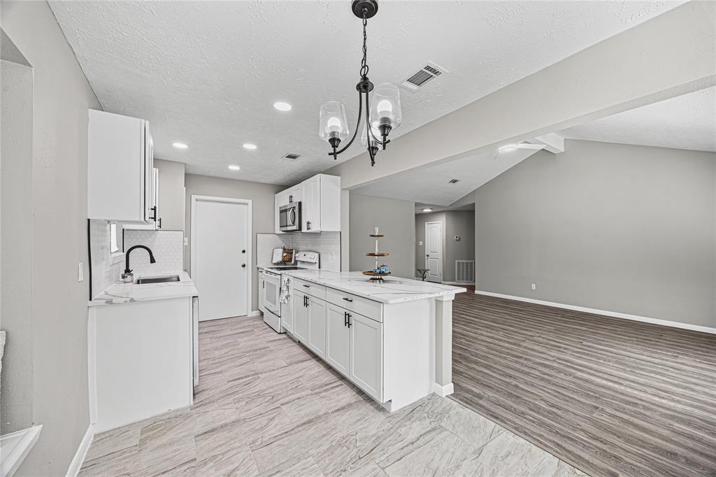 a large white kitchen with stainless steel appliances granite countertop a stove and a wooden floors