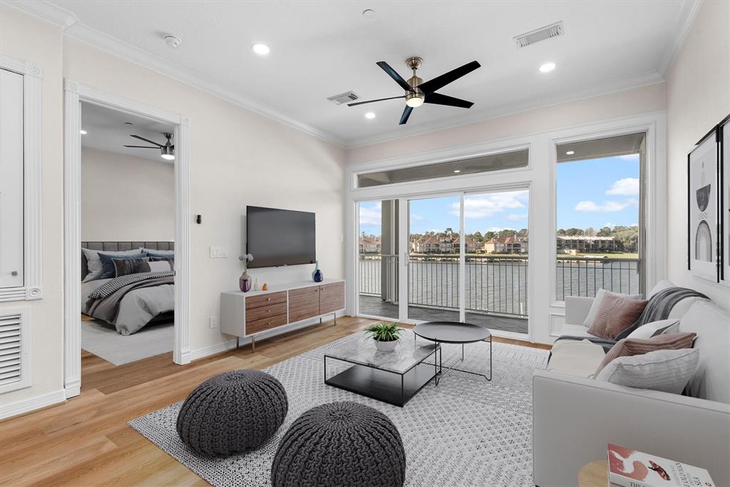 Virtually staged-This is a bright, modern living room with an open floor plan, hardwood floors, and a ceiling fan. It features large windows with a waterfront view, providing plenty of natural light. The room seamlessly connects to a cozy bedroom area.