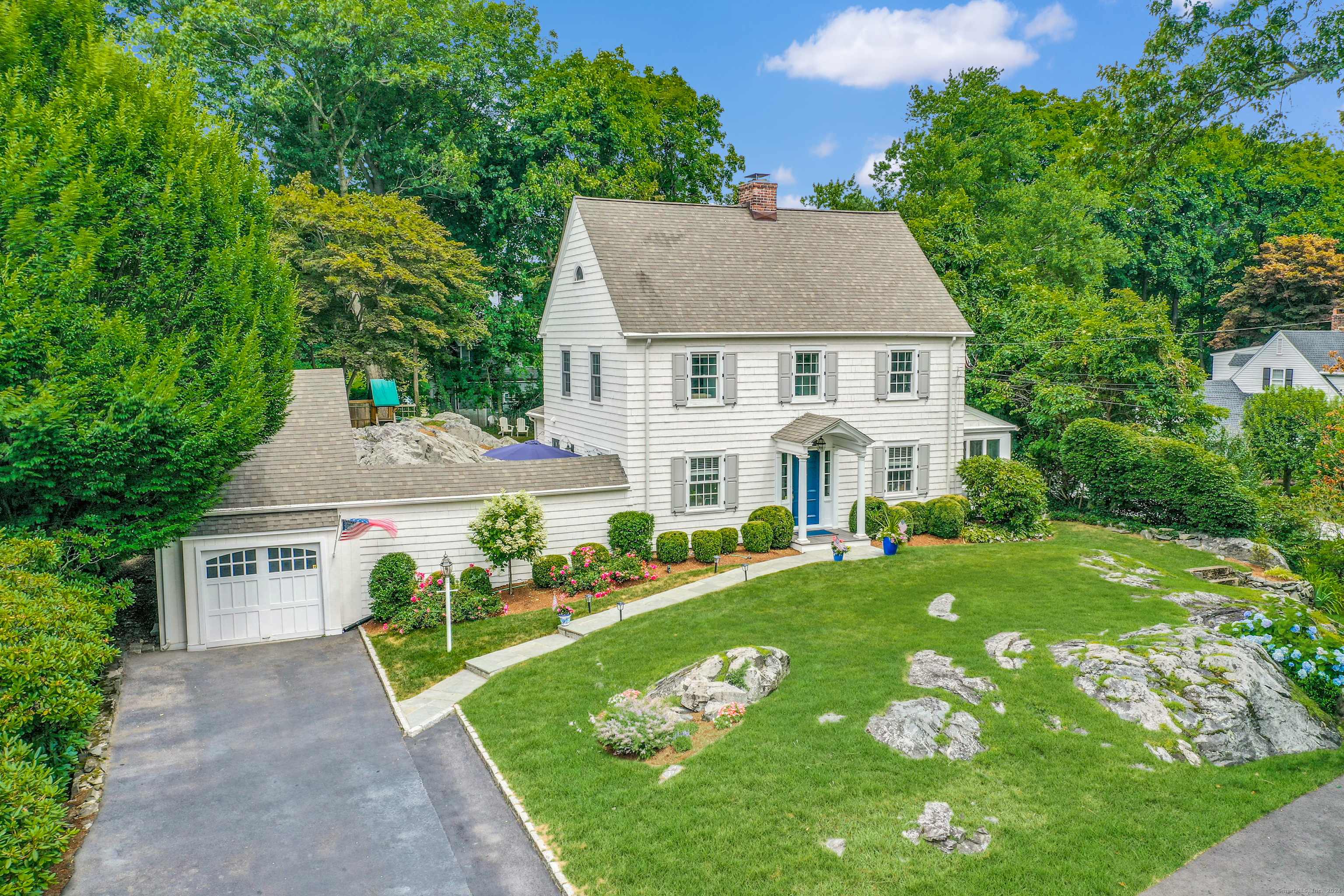 a view of a white house with a yard plants and large tree