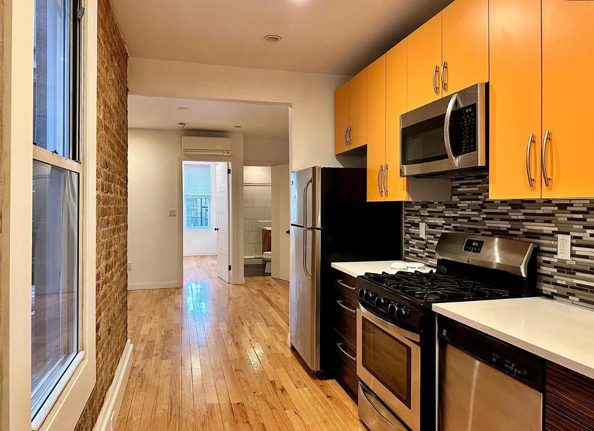 Kitchen featuring stainless steel appliances, a wall unit AC, decorative backsplash, and light wood-type flooring