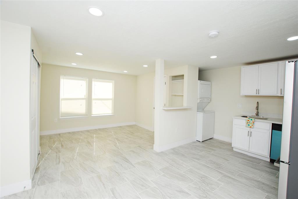 a view of an empty room and kitchen with wooden floor