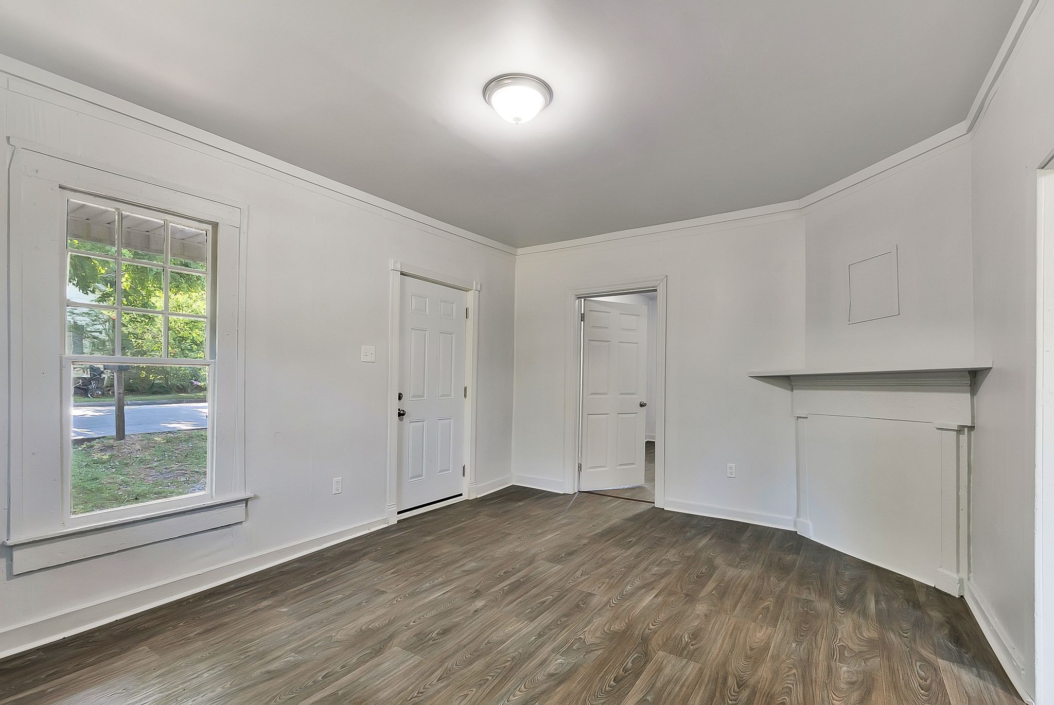 a view of an empty room with wooden floor and a window