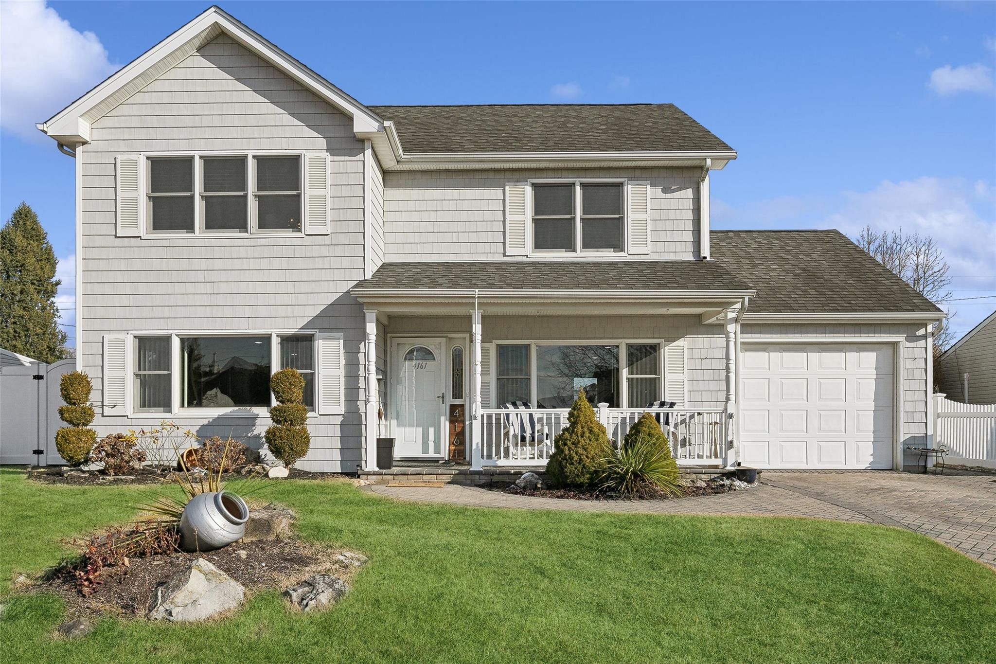 View of property with covered porch, a garage, and a front lawn