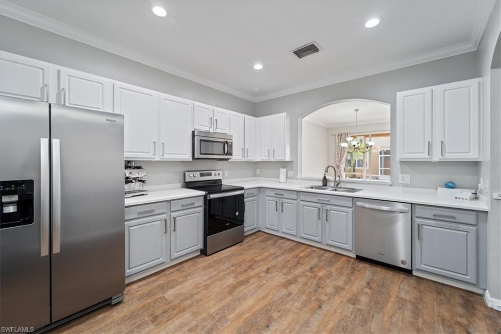 a kitchen with stainless steel appliances granite countertop a refrigerator a sink dishwasher a stove top oven a refrigerator with white cabinets and wooden floor