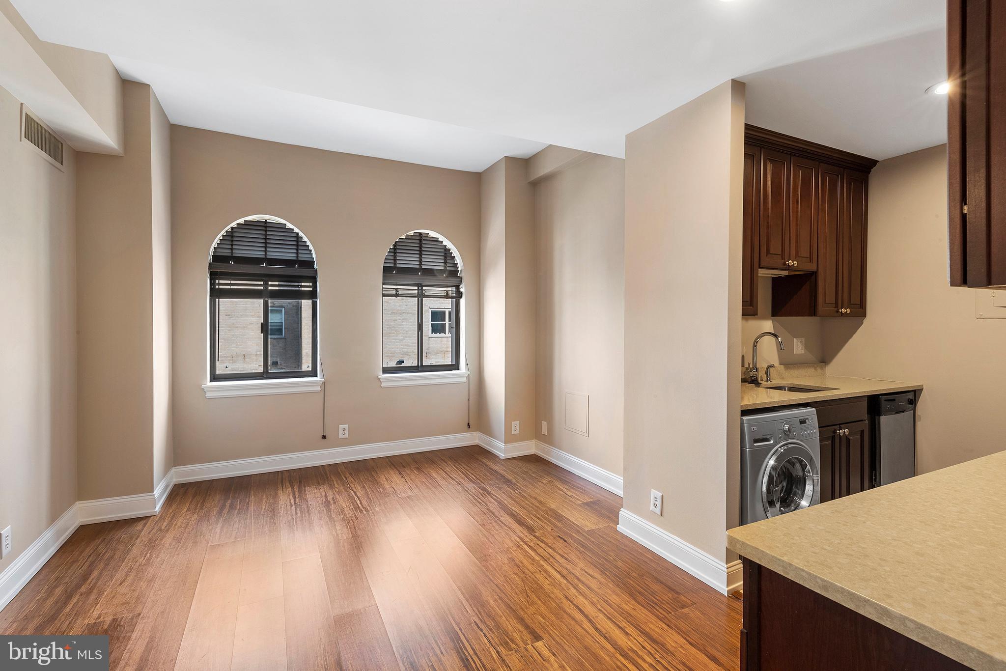 a view of empty room with kitchen view and wooden floor