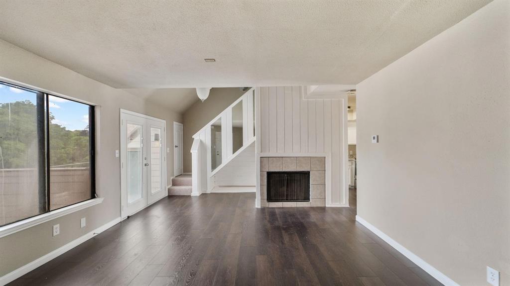 a view of an empty room with wooden floor fireplace and a window