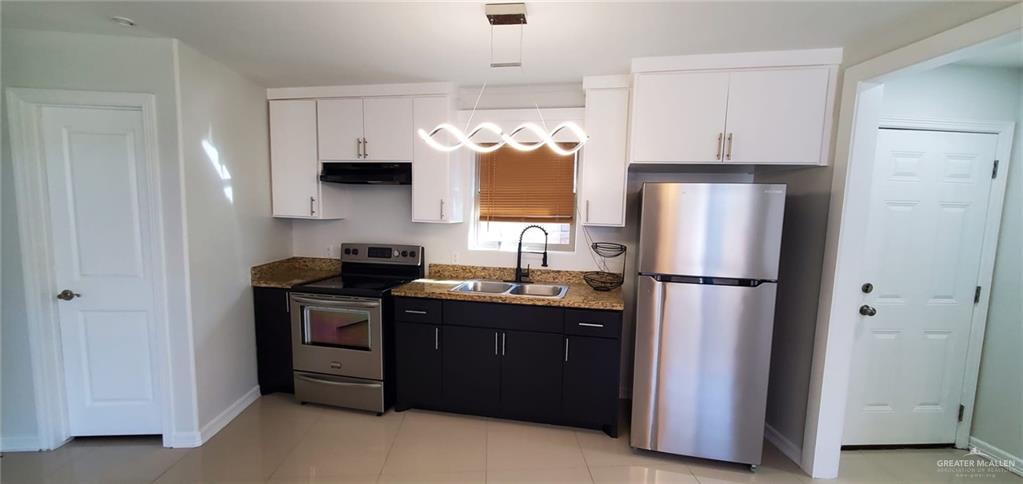 Kitchen featuring dark stone countertops, sink, light tile patterned flooring, white cabinetry, and appliances with stainless steel finishes