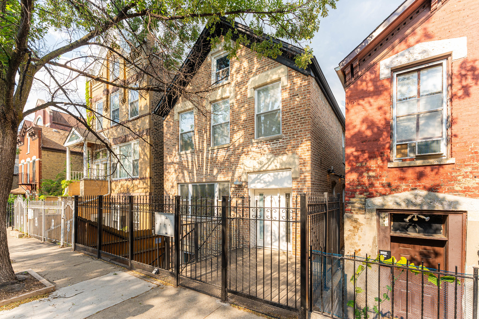 a view of a brick house with a large tree and wooden fence