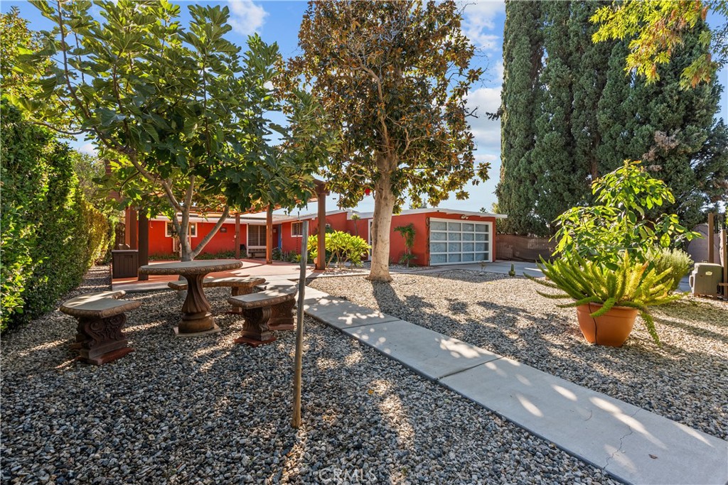 a view of a backyard with table and chairs potted plants and large tree