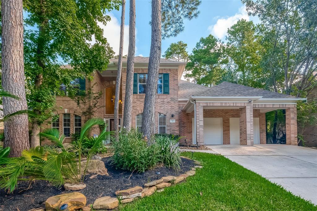 a view of a brick house with a yard plants and large tree