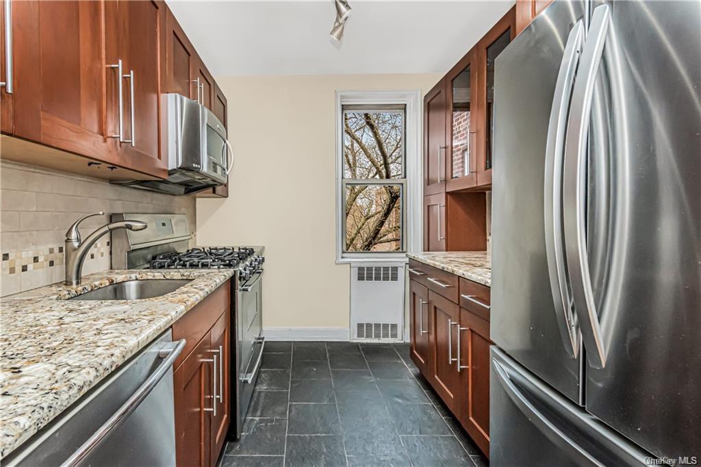 Kitchen with radiator heating unit, tasteful backsplash, light stone counters, appliances with stainless steel finishes, and sink