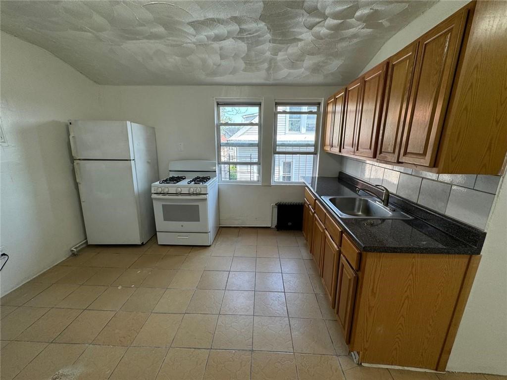 Kitchen with sink, white appliances, backsplash, and light tile patterned floors