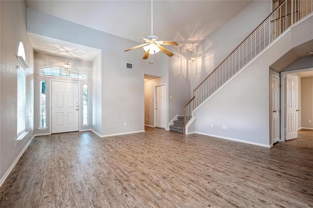 a view of an empty room with wooden floor and a ceiling fan