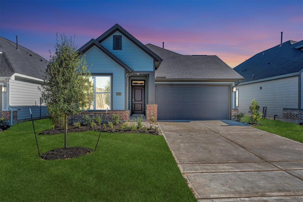 This is a modern, single-story home with a two-car garage. It features a neat front yard with landscaping and a welcoming front entry, set against a picturesque sunset sky.