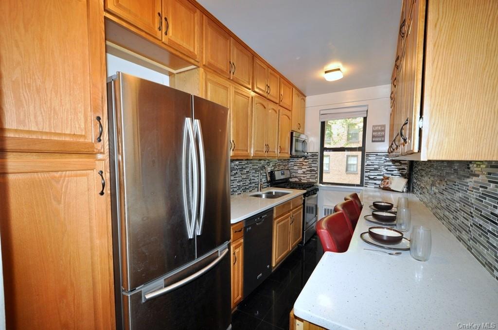 Eat-in-kitchen with Quartz counters and stainless steel appliances including a Dishwasher, Microwave, Range and French Door Refrigerator.  There is a tile backsplash and black galaxy tile floor.