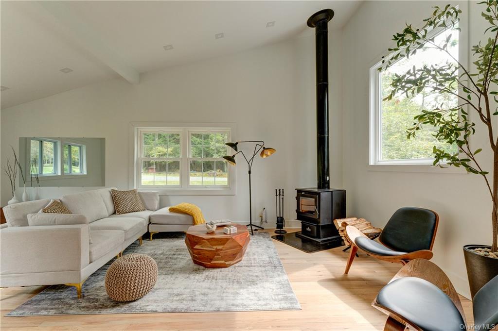 Living room featuring light wood-type flooring, lofted ceiling with beams, and a wood stove